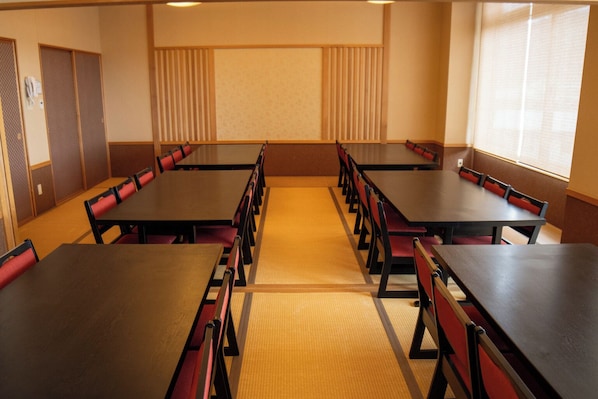 A conference room with multiple tables and chairs, a carpeted floor, and a large window on one side.