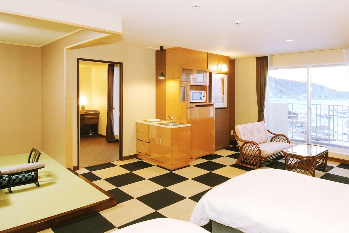 A hotel room with a checkered floor, a bed, a dining table with chairs, a sofa, a TV, and a view of the outdoors.