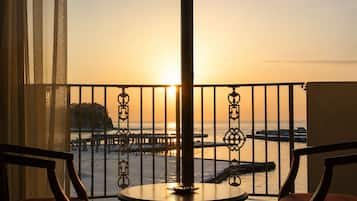 A balcony with a view of the sunset over the water, featuring a table and two chairs.
