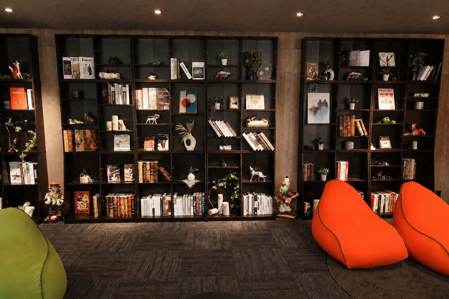 Ein Zimmer mit einer großen Bücherwand, voll mit Büchern und Dekoration, zwei orangenen Sitzsäcken und einem Holzboden.