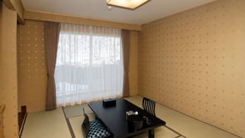 A room with tatami flooring, a black table with chairs, a window with sheer curtains, and a patterned wall.