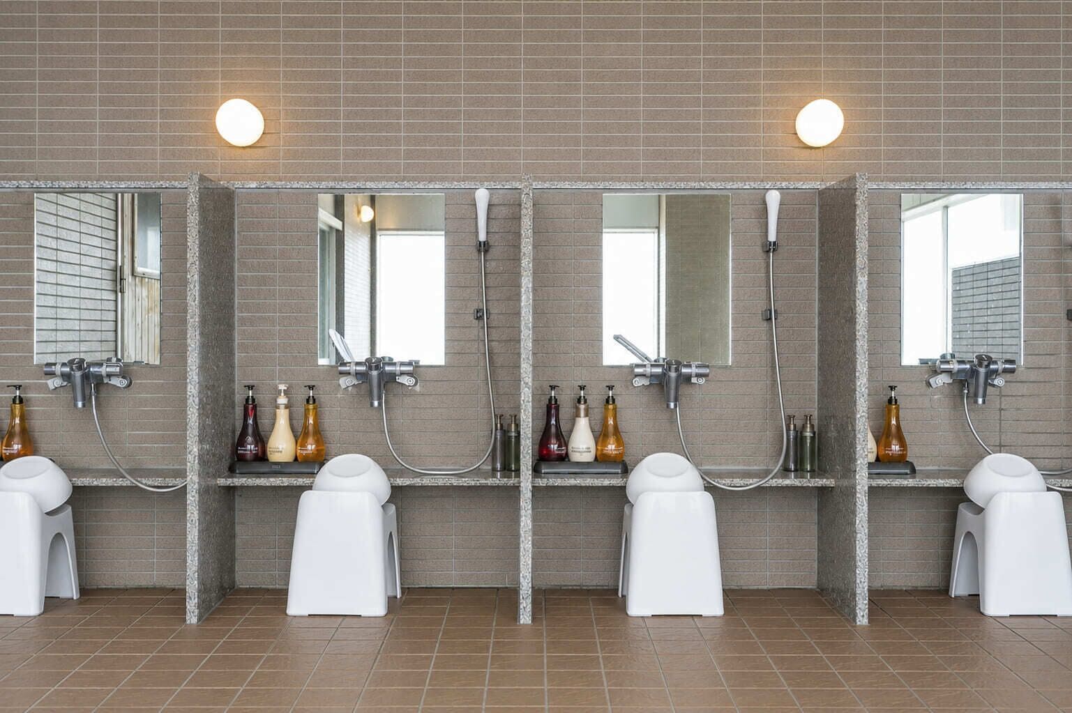 A public restroom with three sinks, each with a mirror and a handheld showerhead.