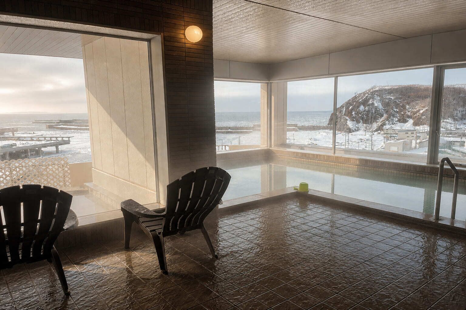 Habitación con un amplio ventanal que da a un paisaje nevado y una zona de piscina con dos sillas.