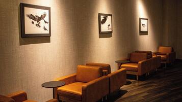 A hotel lobby with leather armchairs, small round tables, and framed wall art.