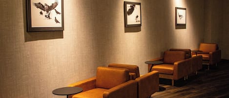 A hotel lobby with leather armchairs, small round tables, and framed wall art.