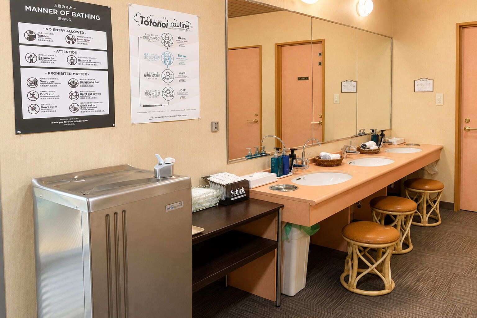 A hotel bathroom with a long vanity, two sinks, a mirror, and a trash bin.