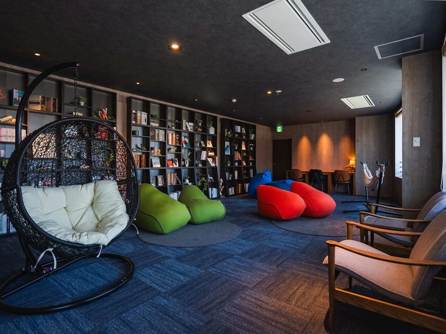 Un área de descanso moderna con una estantería grande, un sillón colgante y pufs de colores.