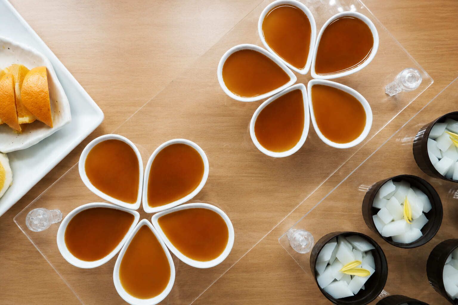 Ein Tisch mit vier Teetassen, die in einem floralen Muster angeordnet sind, ein Teller mit Orangenscheiben und Schalen mit Eiswürfeln und Zitronenscheiben.