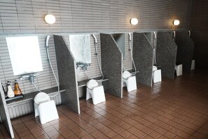 Baño público con varios cubículos, cada uno con espejo, lavamanos e inodoro.