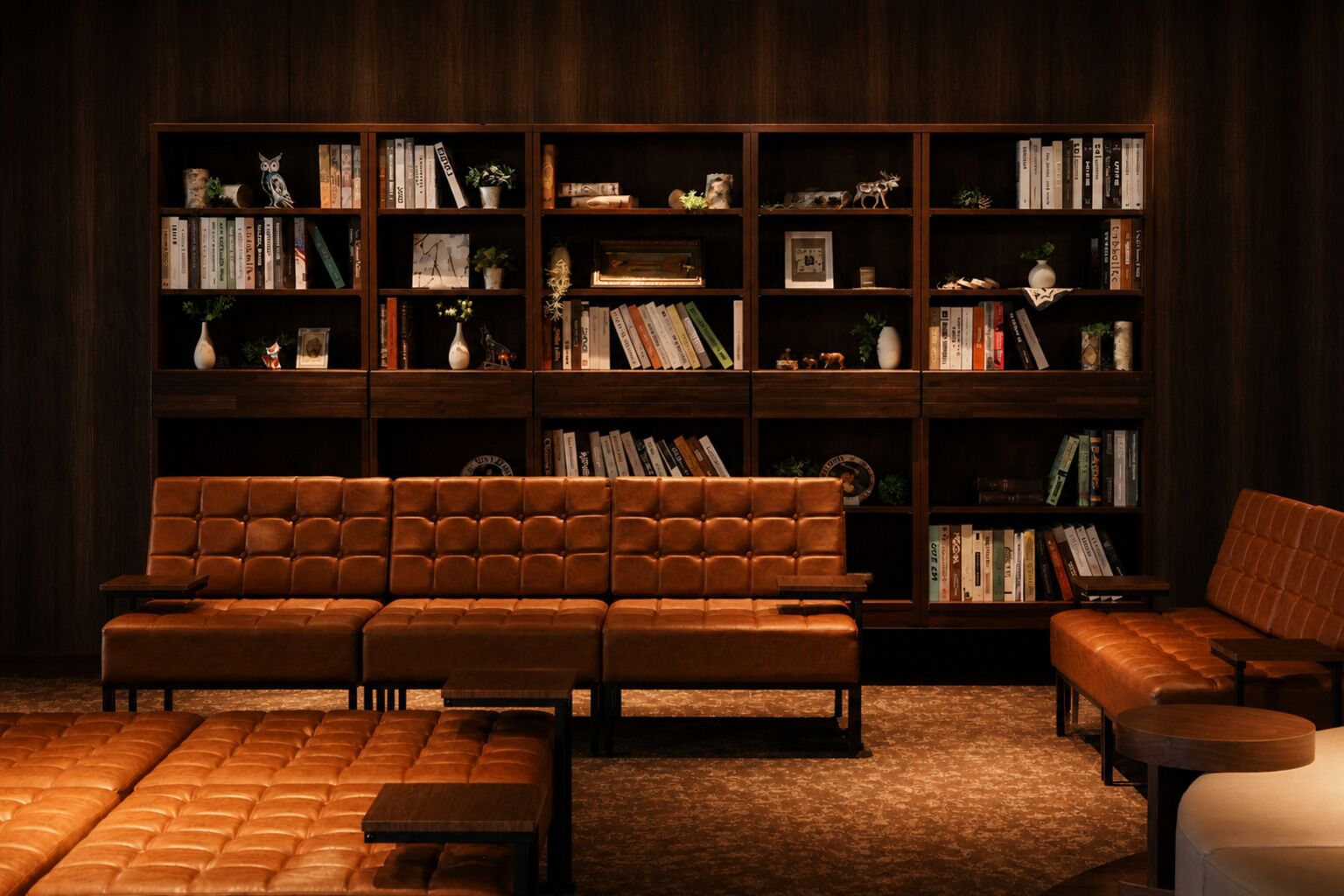 A library with a brown leather sofa, multiple bookshelves, and a carpeted floor.