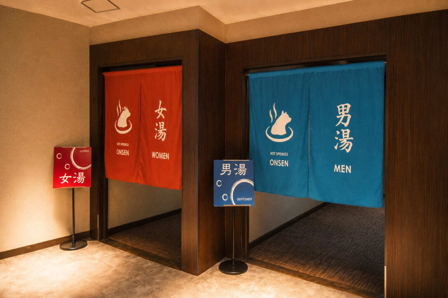 A hotel corridor with separate signs for ladies' and men's hot springs, indicating gender-specific amenities.