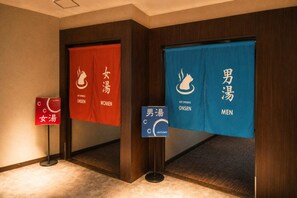 Pasillo de hotel con indicaciones separadas para aguas termales de mujeres y hombres, señalando servicios exclusivos por género.