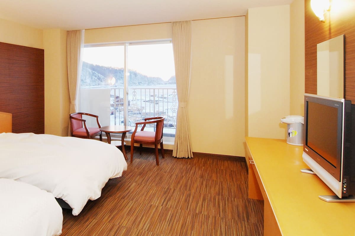 A hotel room with two beds, a TV, a desk, and a chair.