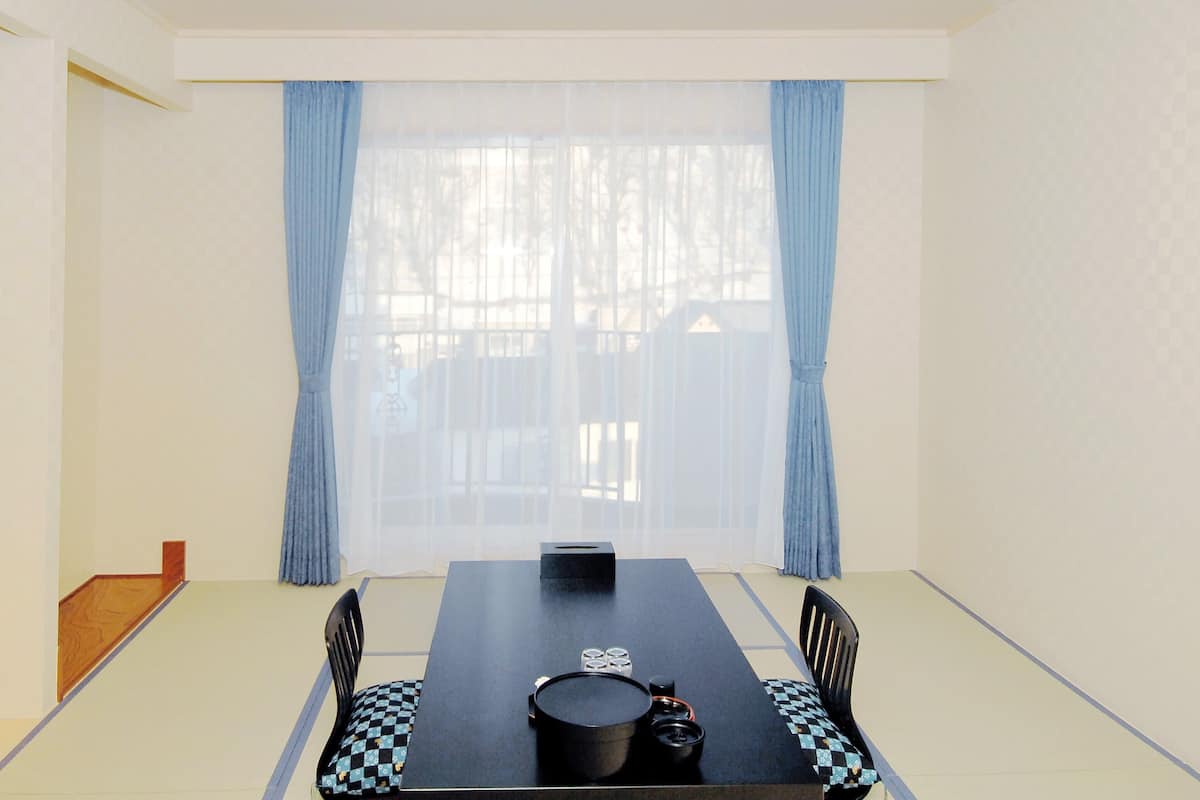 A room with a dining table, chairs, a television, and a window with curtains.