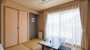 Une pièce avec un sol recouvert de tatamis, une petite table basse, un radiateur et une fenêtre ornée de rideaux légers.