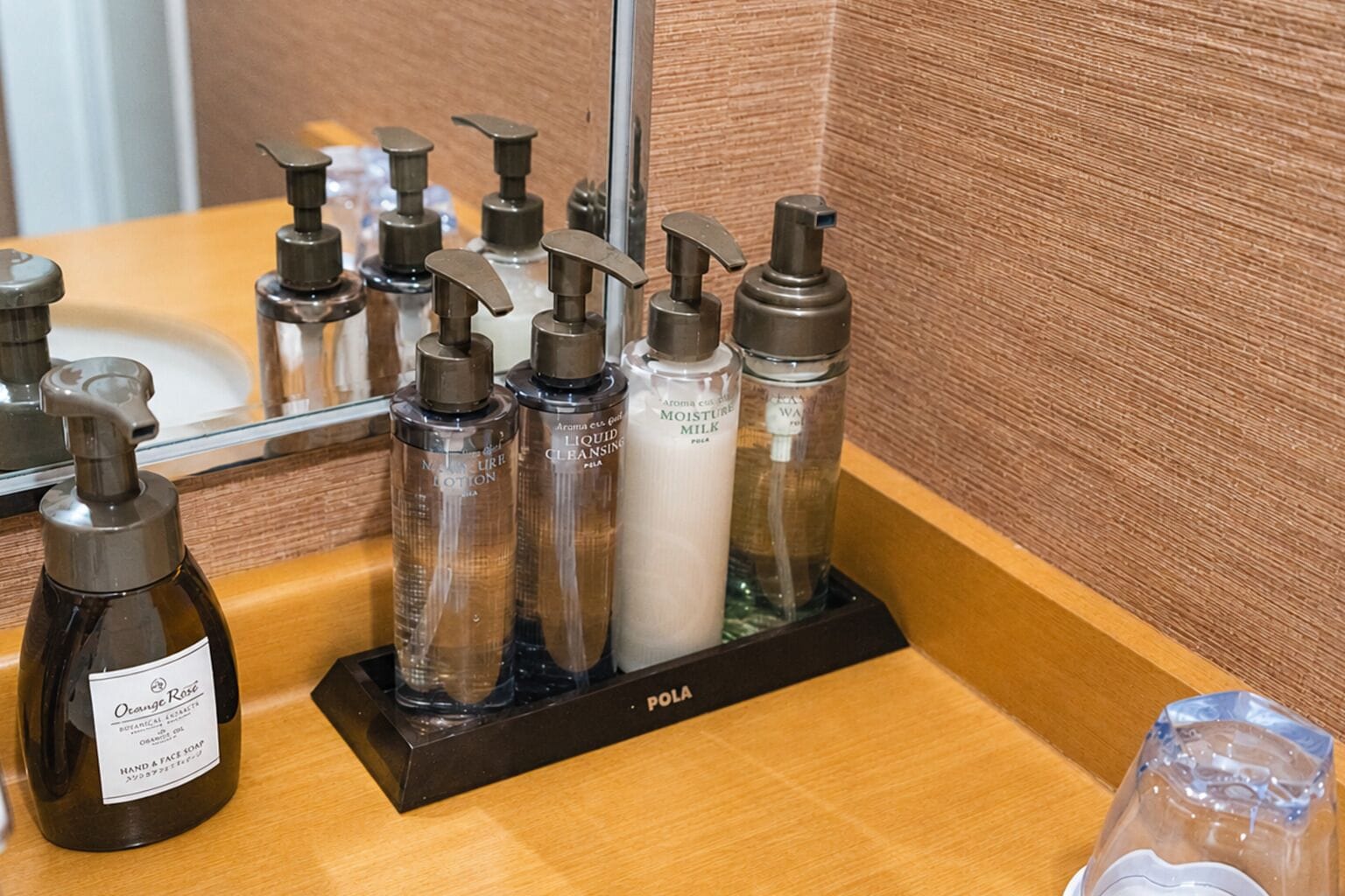 A bathroom vanity with a mirror, a soap dispenser, and a bottle of hand & face soap.