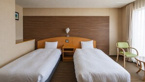 Une chambre d’hôtel avec deux lits simples, une tête de lit en bois, une petite table, une chaise verte et un tableau au mur.