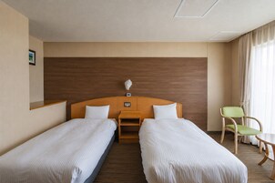 Habitación de hotel con dos camas individuales, cabecera de madera, una mesita, una silla verde y un cuadro en la pared.