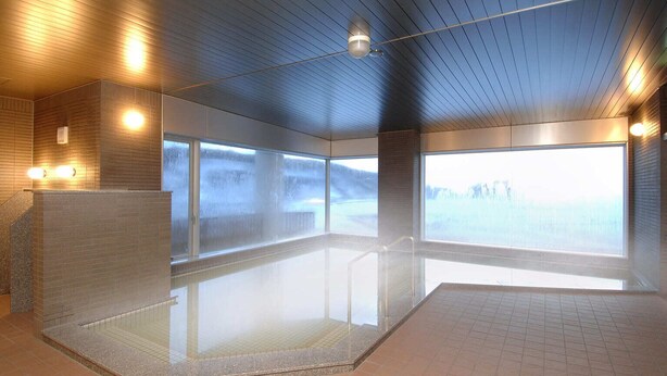 Un espace piscine intérieur moderne, doté de parois en verre transparent, d’un sol carrelé et d’un plafond équipé de luminaires linéaires.