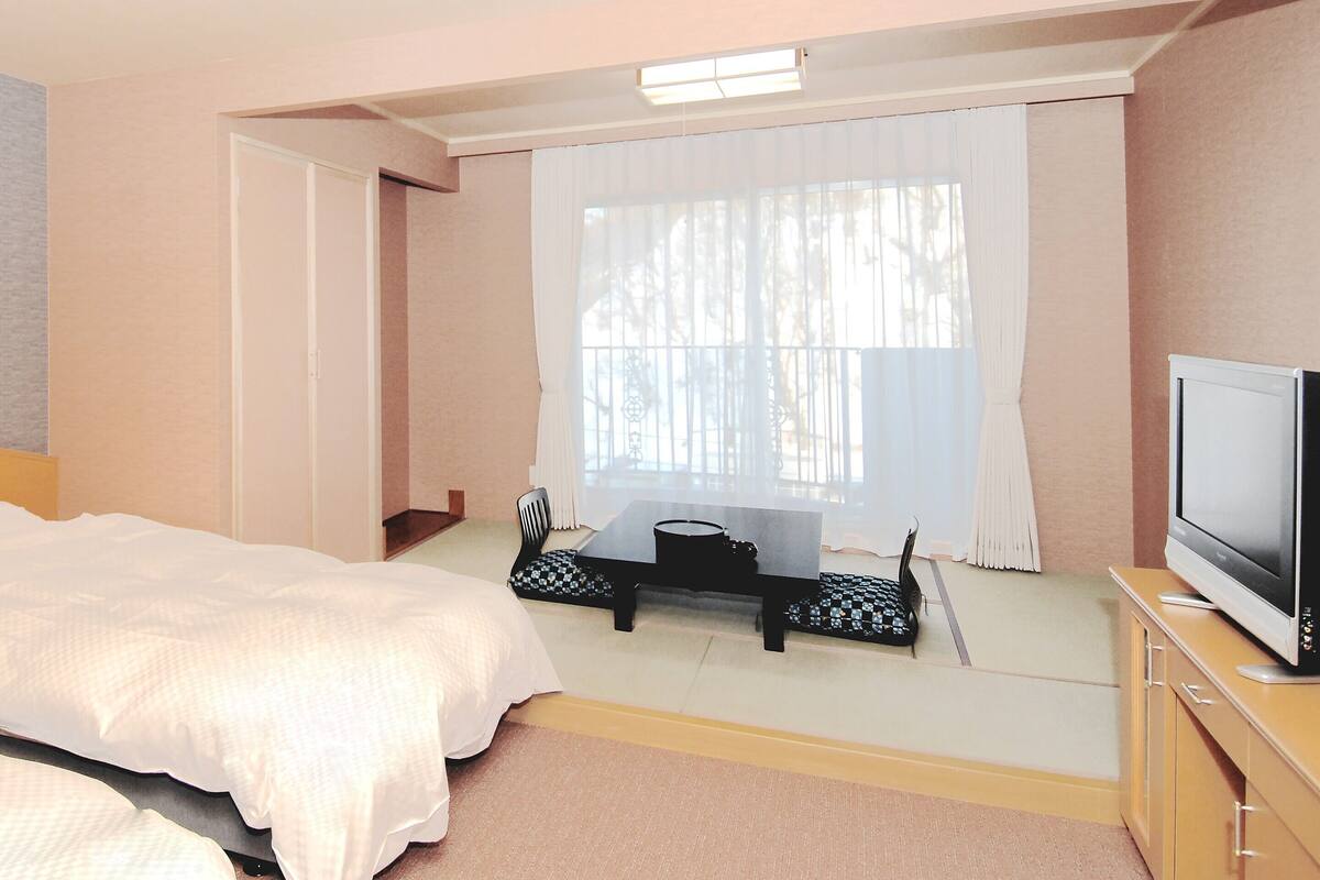 A hotel room with two beds, a desk with a telephone, a television, and a window with curtains.