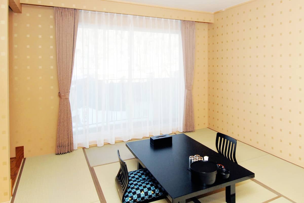 A room with tatami flooring, a black table with a black box, two black chairs, and a window with sheer curtains.