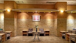 Un hall d’entrée aux murs en pierre, une table ronde centrale entourée de chaises et un tableau encadré accroché au mur.