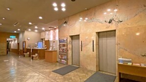 Un hall d’hôtel comprenant un comptoir d’accueil, un terminal en libre-service, une petite boutique et un ascenseur.