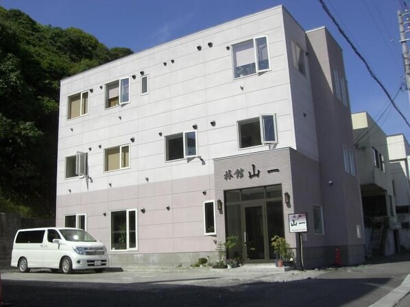 A multi-story building with a modern design, featuring a sign with Japanese characters and a small entrance area with potted plants. - Ryokan Yamaichi (Wakkanai)