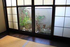 Habitación con suelo de tatami, pantalla de shoji y un pequeño jardín interior con plantas y rocas.