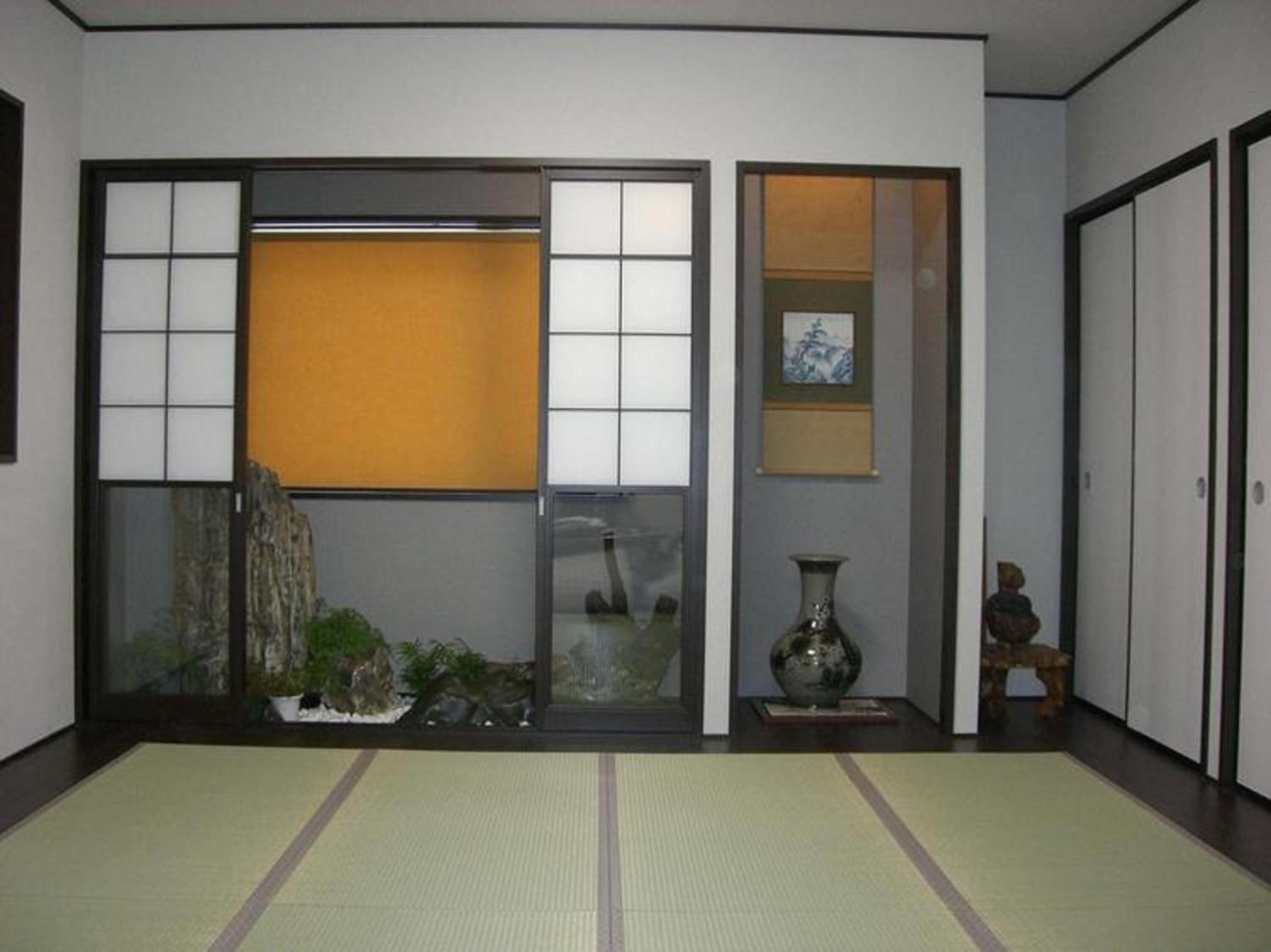 Une pièce de style japonais traditionnel, avec un sol recouvert de tatamis, des portes coulissantes, un paravent shoji, un petit jardin intérieur et un vase posé sur une table.