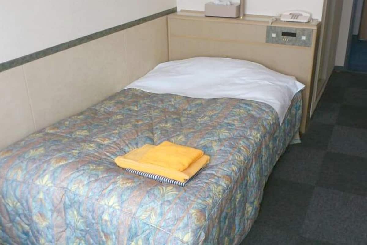 Una cama individual con una colcha estampada, una almohada blanca y una toalla amarilla doblada.