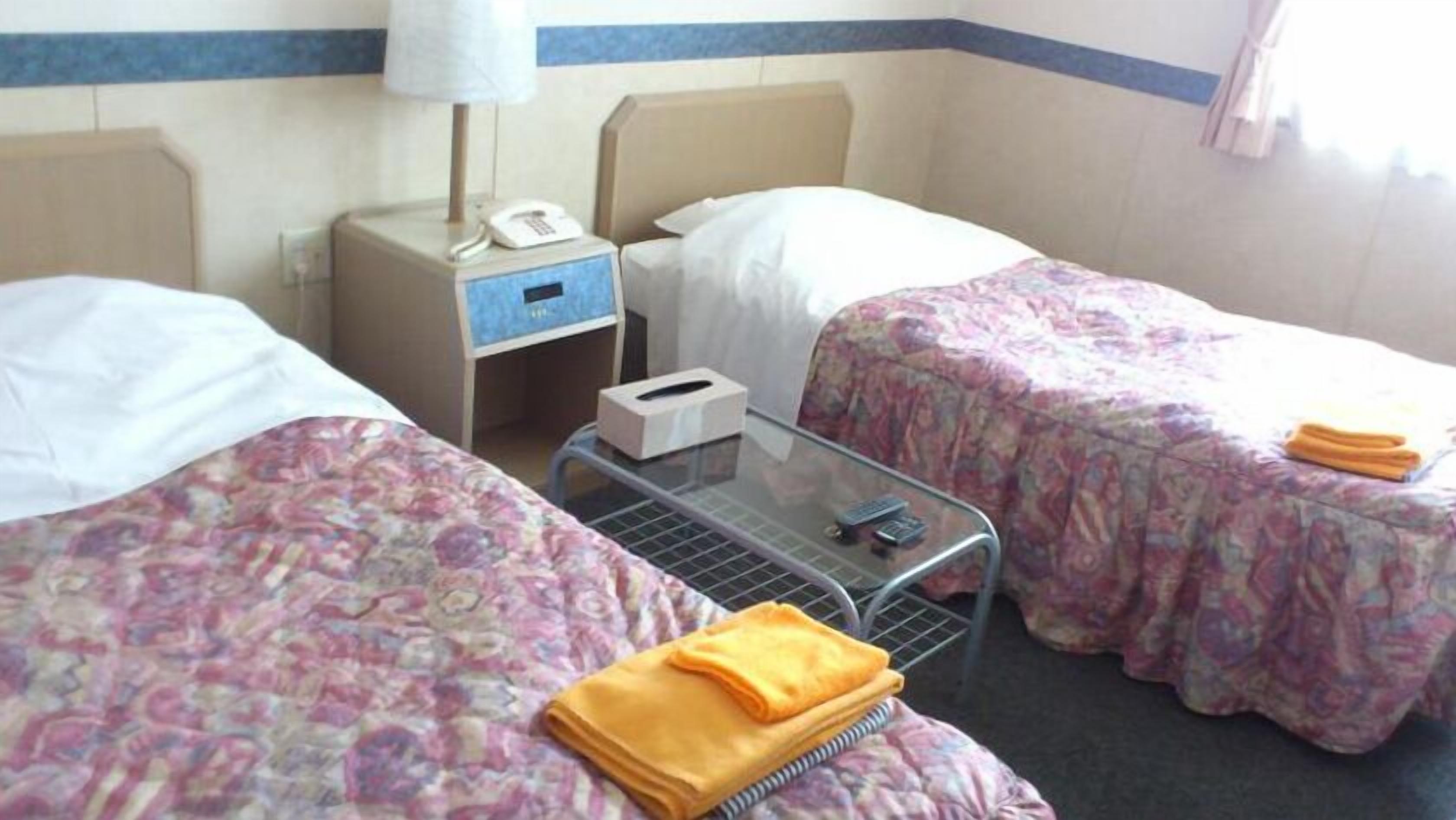 A hotel room with two beds, a bedside table with a lamp, a telephone, and a tissue box.
