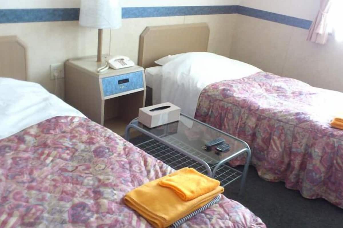 Une chambre d’hôtel avec deux lits, une table de chevet avec une lampe, un téléphone et une boîte de mouchoirs.