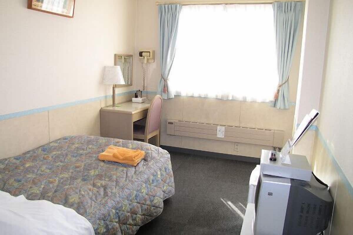 Habitación de hotel con cama, escritorio, silla, televisor y ventana con cortinas.