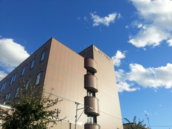 Un edificio alto de diseño moderno, con una estructura vertical destacada y un cielo despejado con nubes.