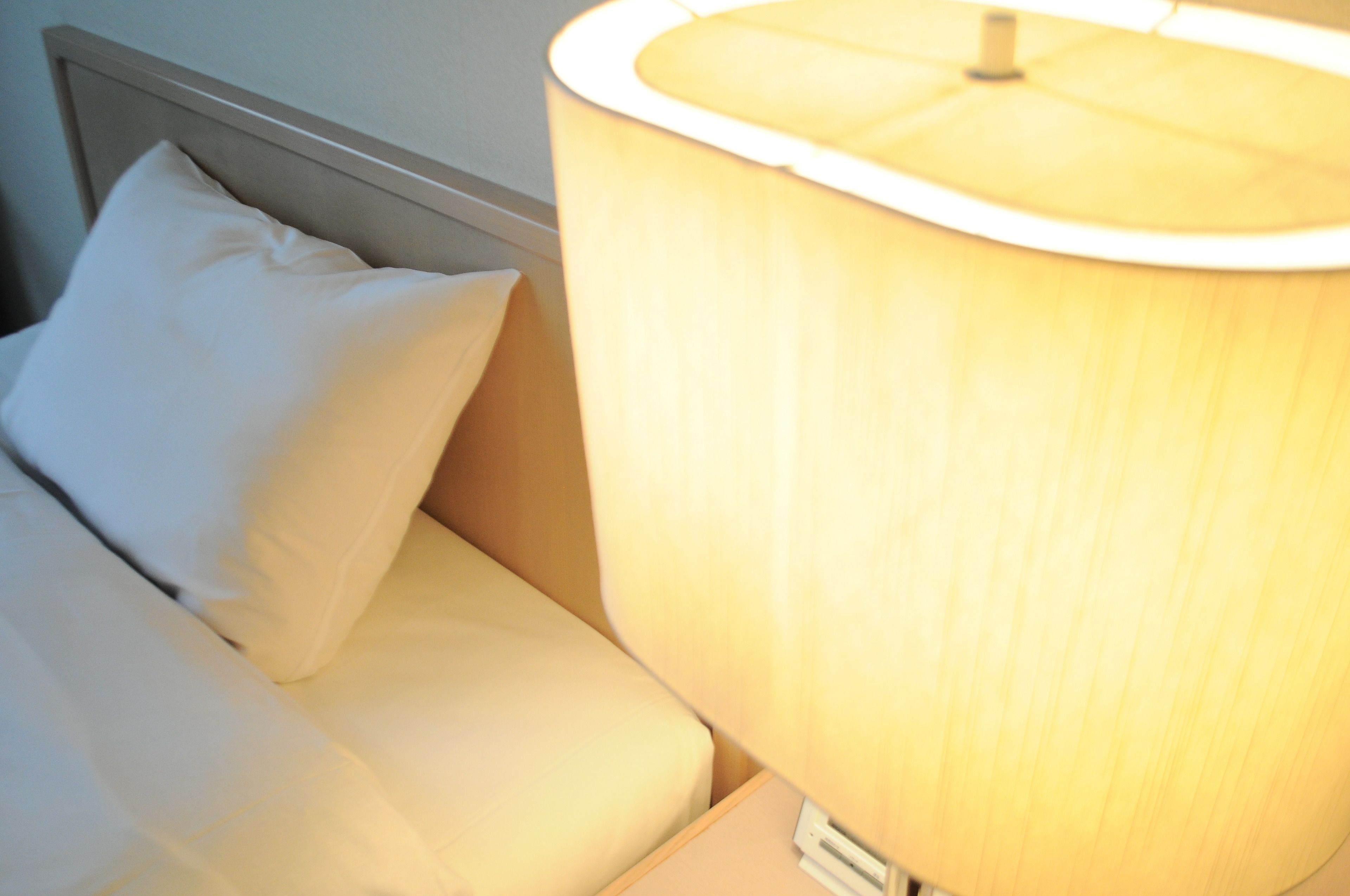 A bed with white bedding and a lamp with a beige lampshade.