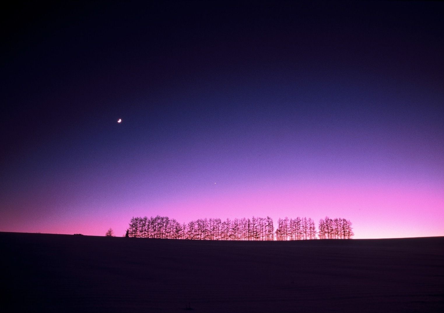 A night sky with a crescent moon and a pinkish hue near the horizon.