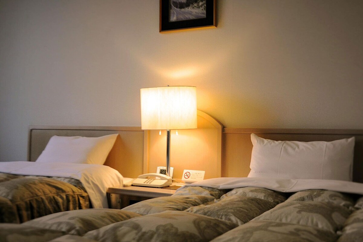 A hotel room with a bed, a bedside lamp, a phone, and a sign indicating no smoking.