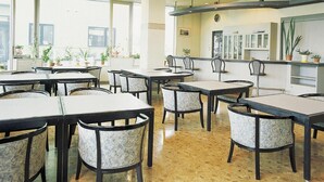 A spacious indoor dining area with multiple tables and chairs, large windows allowing natural light, and potted plants adding greenery. - Hotel Sunfuraton (Furano)