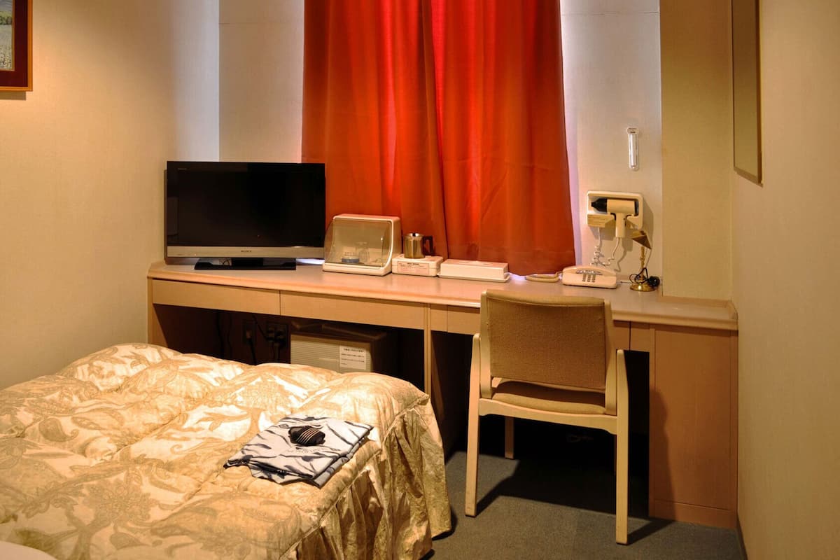 A hotel room with a bed, a desk with a television, a laptop, and a chair.