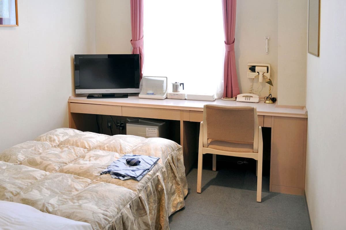 A hotel room with a bed, a desk with a television, a chair, and a window with curtains.