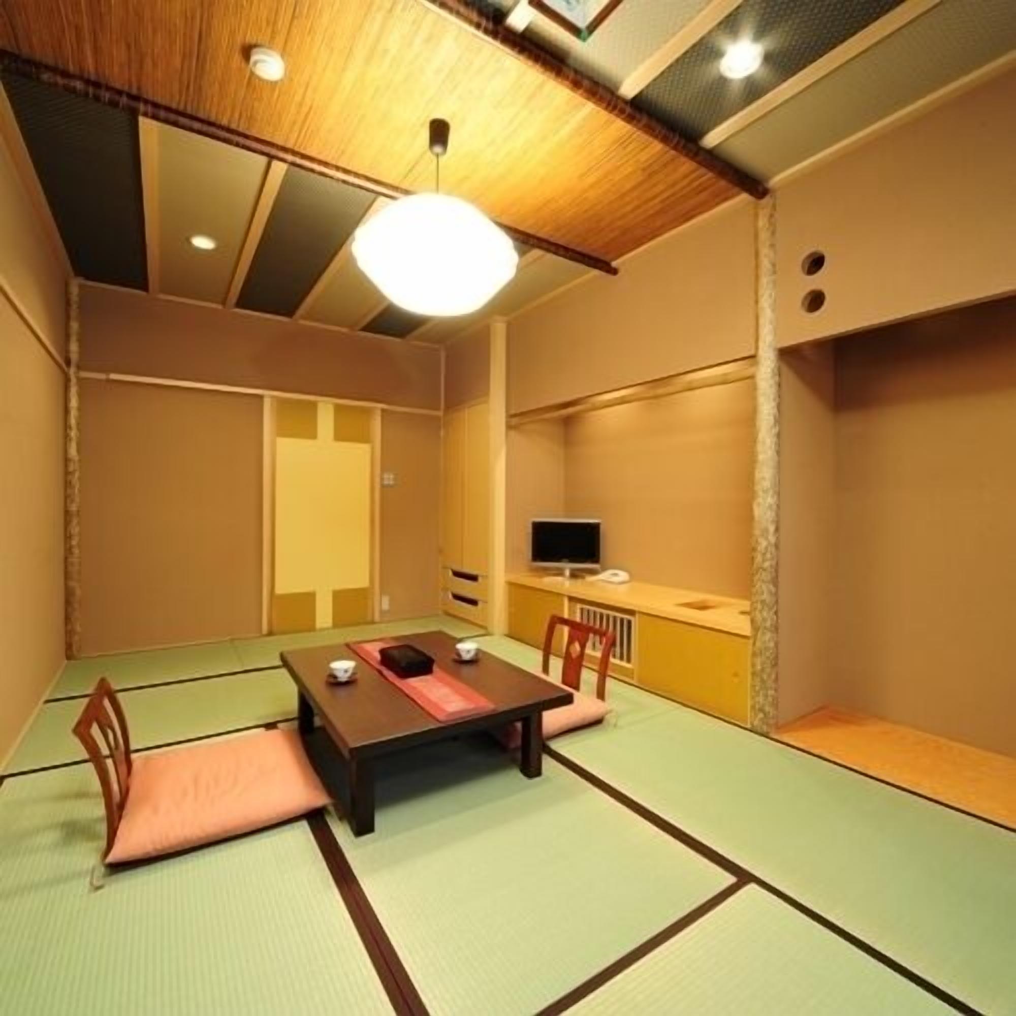Una habitación con esterillas tatami, una mesa baja, sillas, un televisor y una lámpara en el techo.