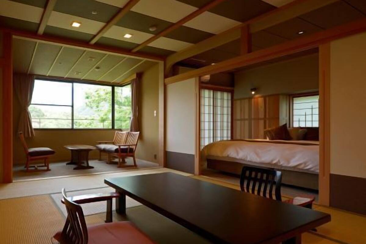 A traditional Japanese-style room with tatami flooring, a low table, chairs, and a bed with a futon.