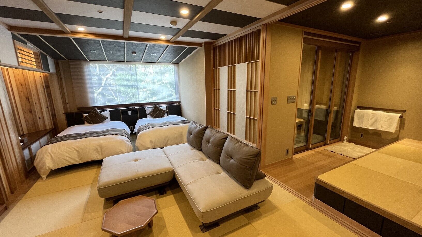 A room with a sofa, two beds, a sliding door, and a window.