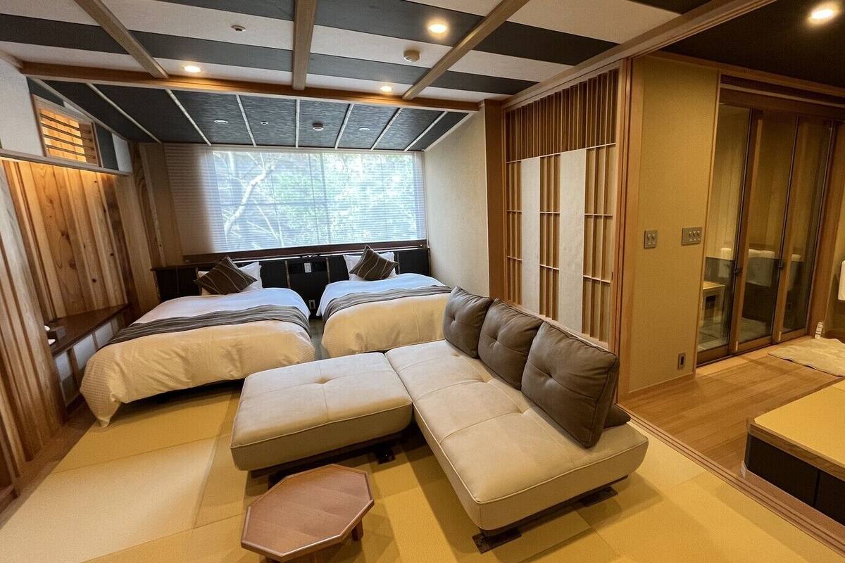 A room with a sofa, two beds, a sliding door, and a window.