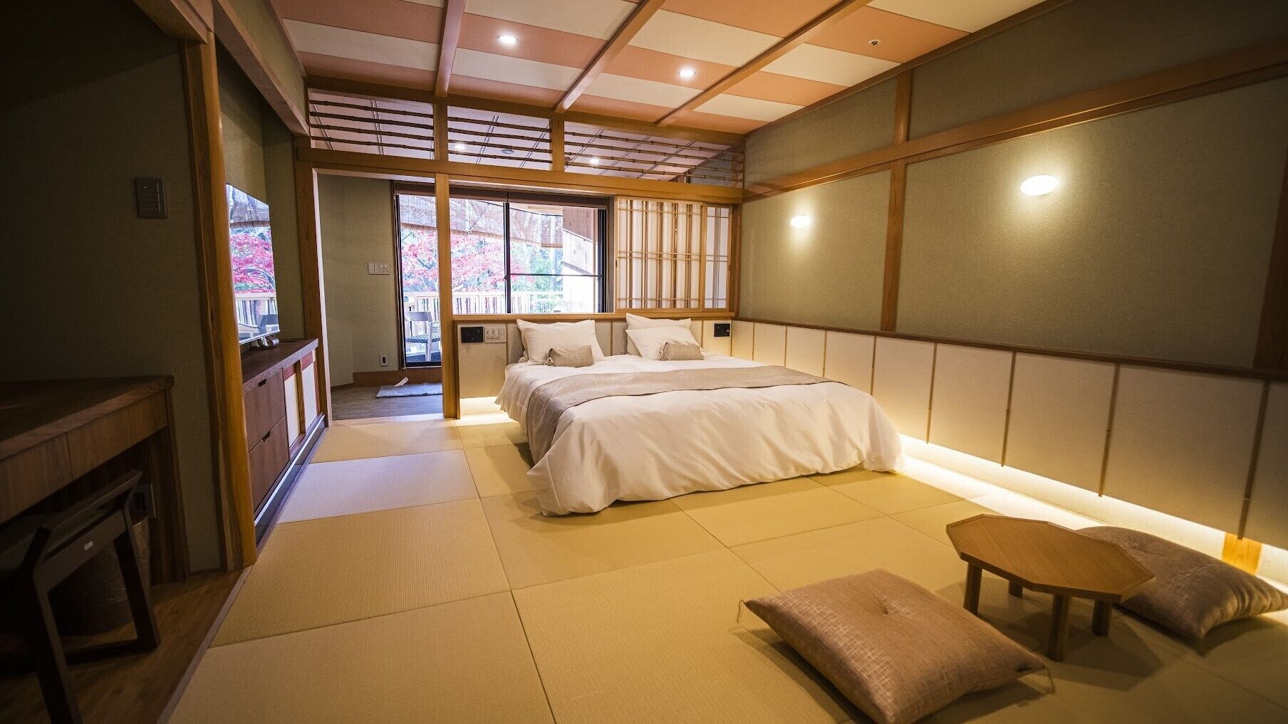 Un dormitorio japonés tradicional con suelo de tatami, una cama con ropa de cama blanca, una pequeña mesa de madera y vistas a flores de cerezo a través de la ventana.