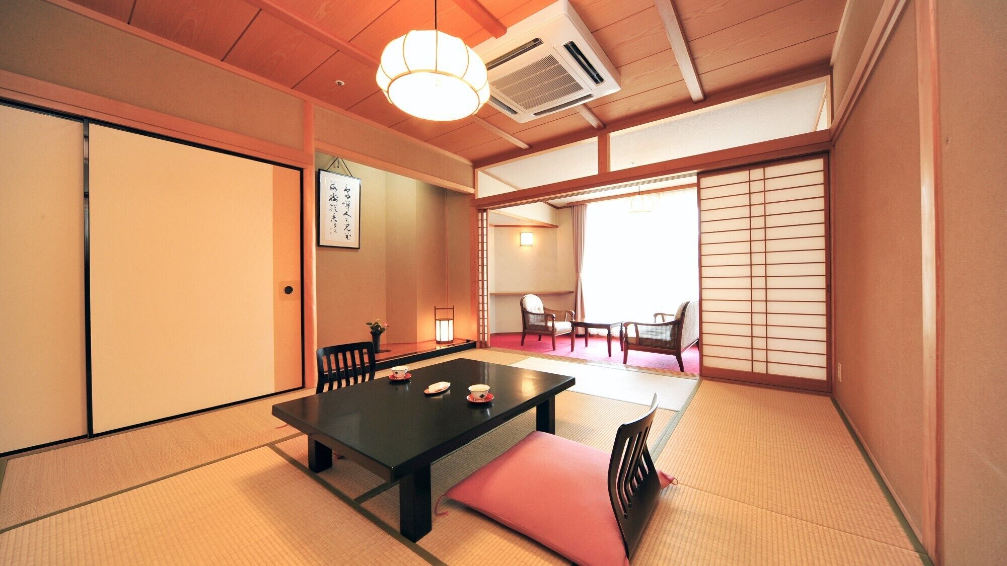 Una habitación tradicional japonesa con suelo de tatami, una mesa baja con cojines, una puerta corredera y vistas a un jardín a través de un celosía shoji.