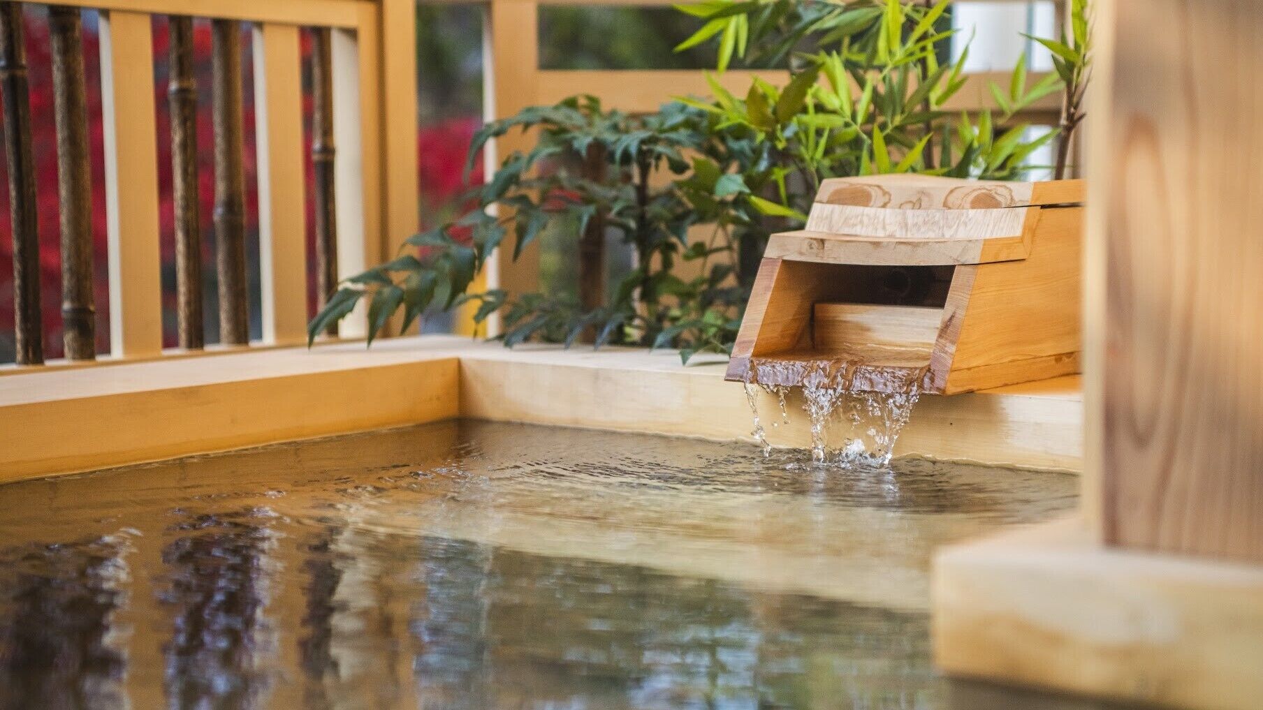A wooden water feature with a small waterfall, surrounded by plants and a wooden bench.