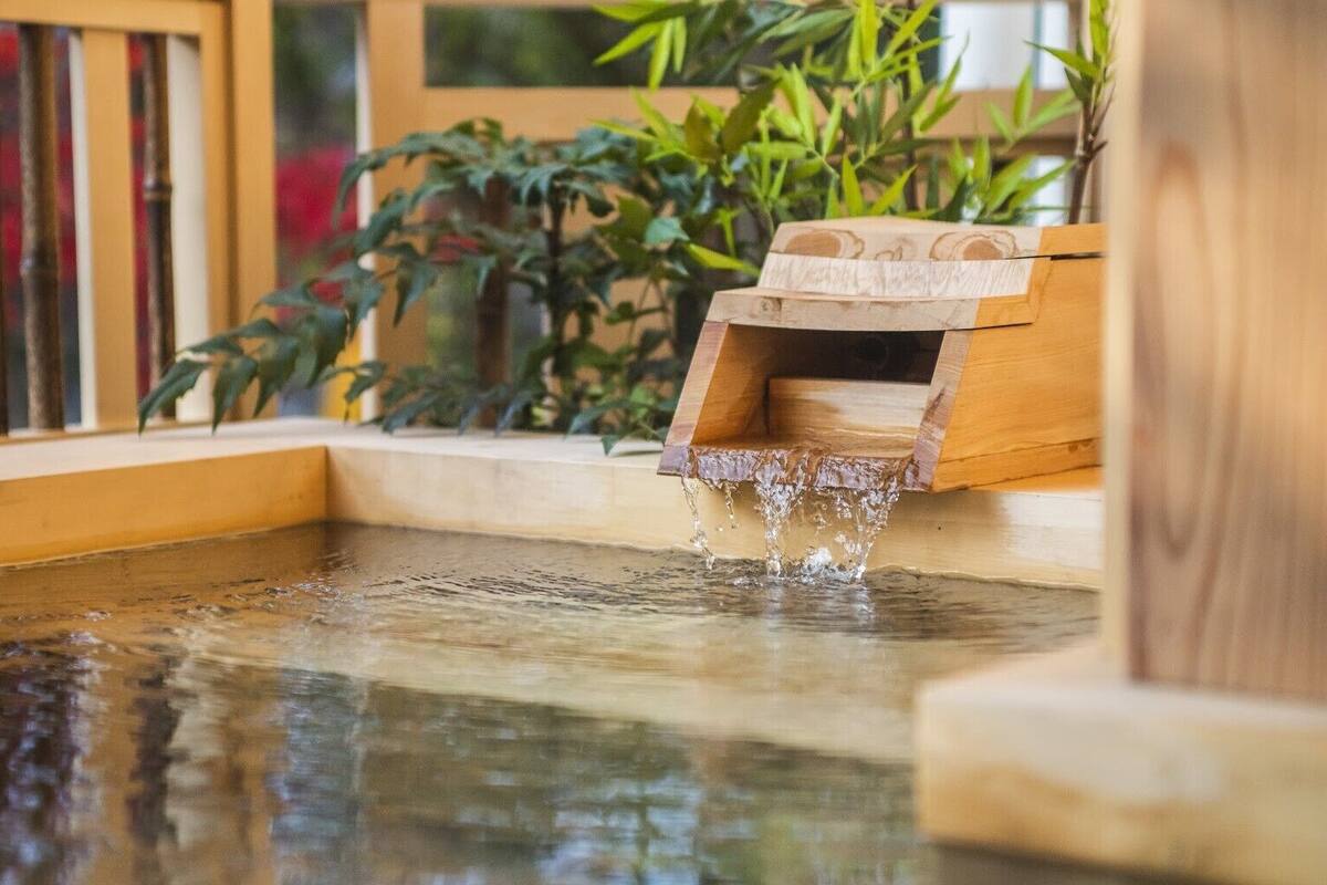 A wooden water feature with a small waterfall, surrounded by plants and a wooden bench.