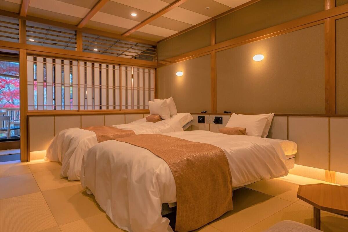 A traditional Japanese-style room with tatami flooring, a low wooden bed with white bedding, and a sliding shoji screen door.